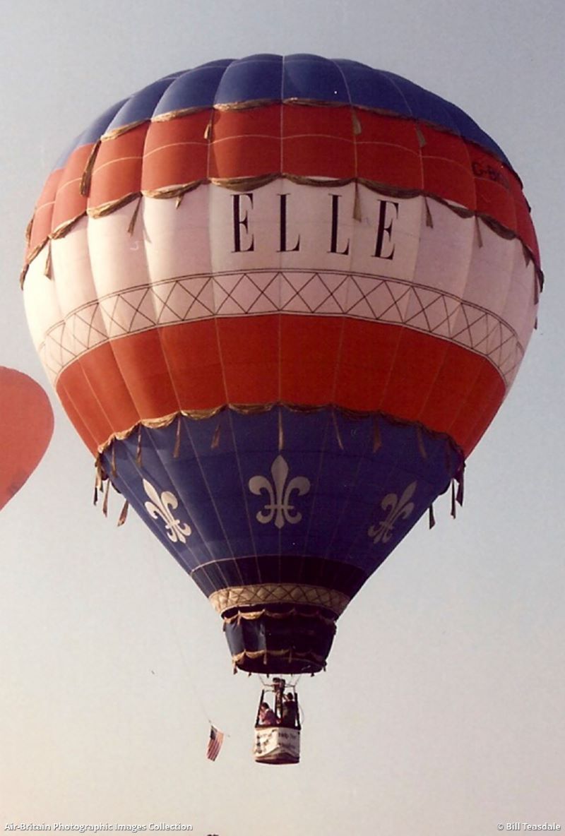 Balloon airborne with horizontal stripes in blue, red, white, red, blue with fleur de lys motifs around lower blue panel and the name ELLE in black on the white centre panel.